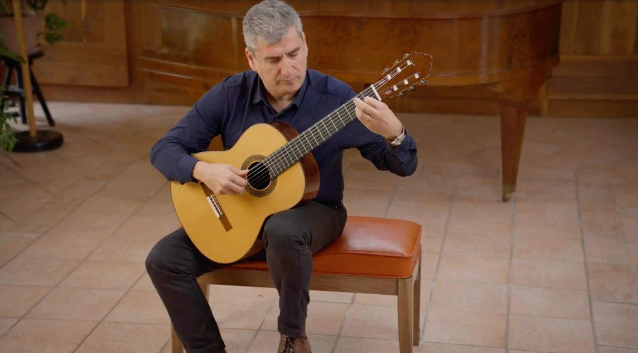 Alexandre Bernoud playing guitar, seated in a navy shirt in front of a piano