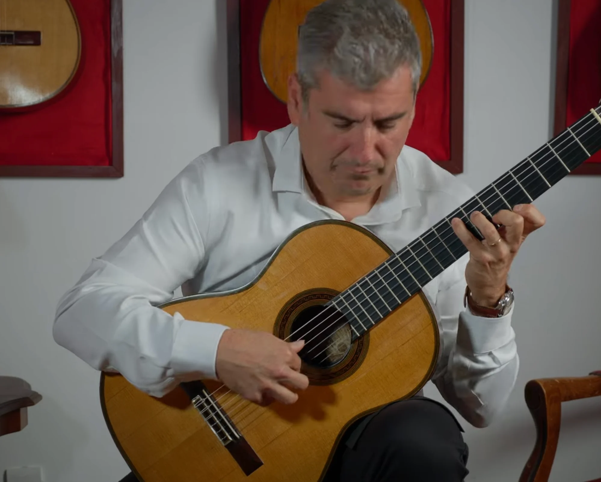 Alexandre Bernoud playing guitar in a white shirt against red panels